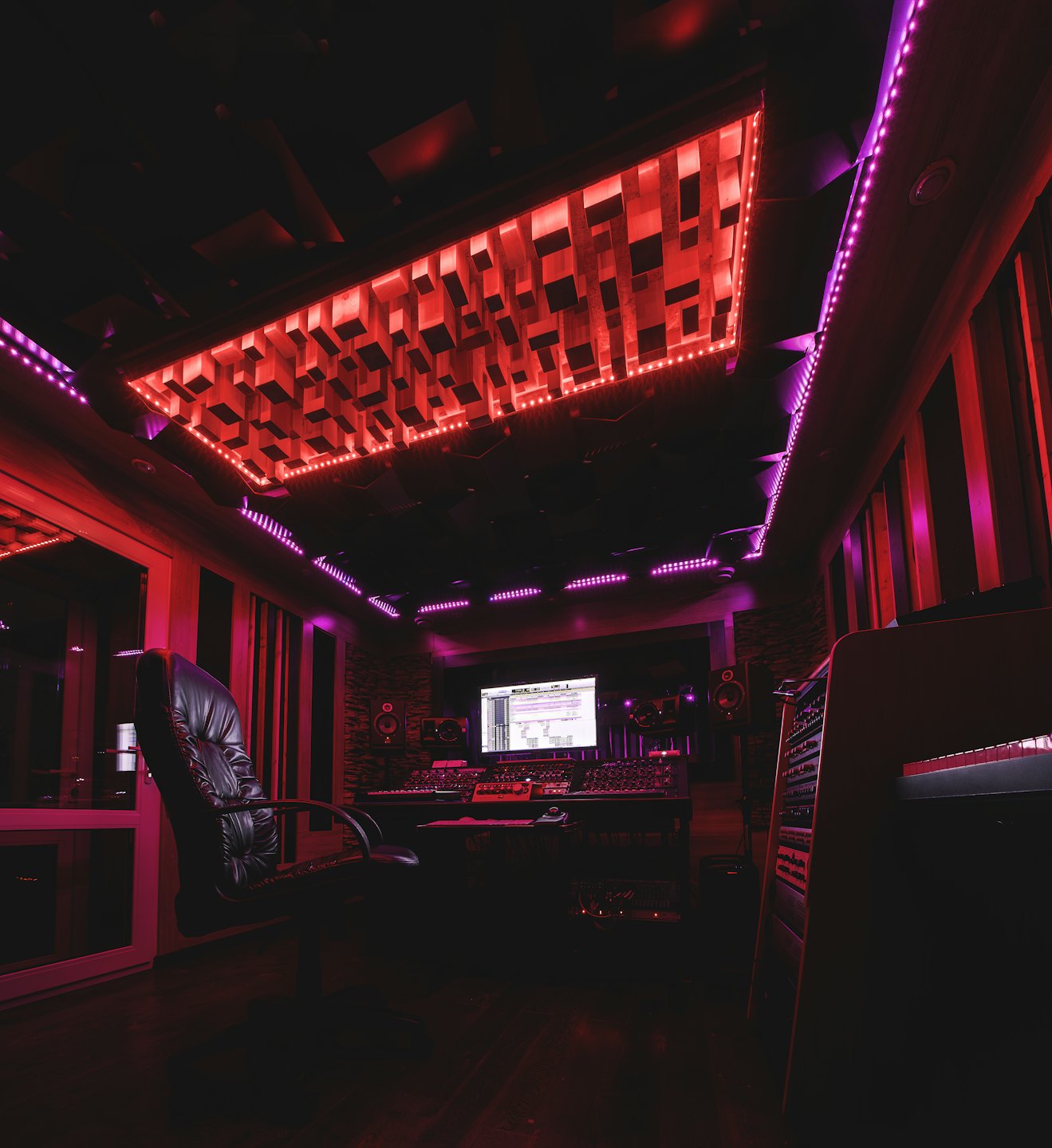 Studio di registrazione vuoto con attrezzatura audio illuminato da luci rosse e viola.